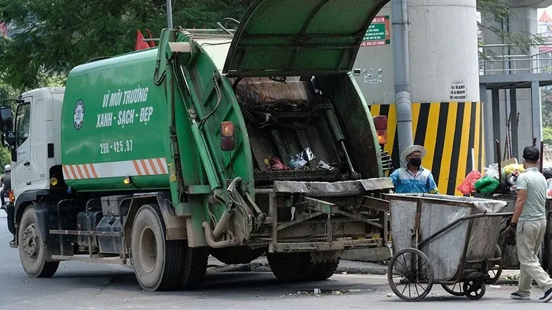 Chủ đề hình ảnh tập trung vào việc phân loại và thu gom chất thải rắn xây dựng tại công trường với các thùng chứa được dán nhãn rõ ràng theo từng loại vật liệu như bê tông, kim loại, gỗ và rác thải hỗn hợp. Các công nhân mặc đồng phục, đeo găng tay và mũ bảo hộ đang thực hiện công việc phân loại một cách cẩn thận. Xa xa là các máy móc thiết bị hỗ trợ công tác thu gom. Bối cảnh là một công trường xây dựng đang hoạt động, có thể có một phần công trình đang được thi công.